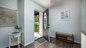 Un pasillo con un banco de madera, una puerta blanca con un cartel de 'Welcome', un mapa mundial y un cuadro con flores.