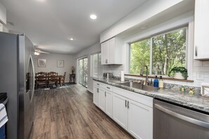 Una cocina moderna con armarios blancos, encimera de granito y un ventanal con vistas a árboles.