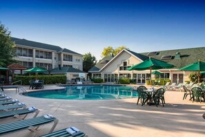 A swimming pool area with lounge chairs and umbrellas, surrounded by buildings with a modern design.