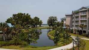 A residential area with a pond, greenery, and a multi-story building with balconies.