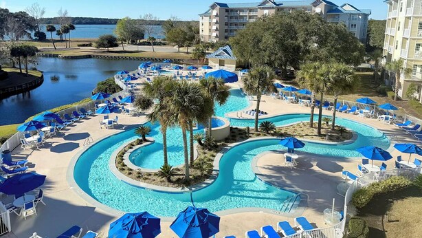 A resort pool area with multiple swimming pools, lounge chairs, and umbrellas.
