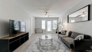 Een moderne woonkamer met een flatscreen televisie, een ronde salontafel, een bank en een plafondventilator.