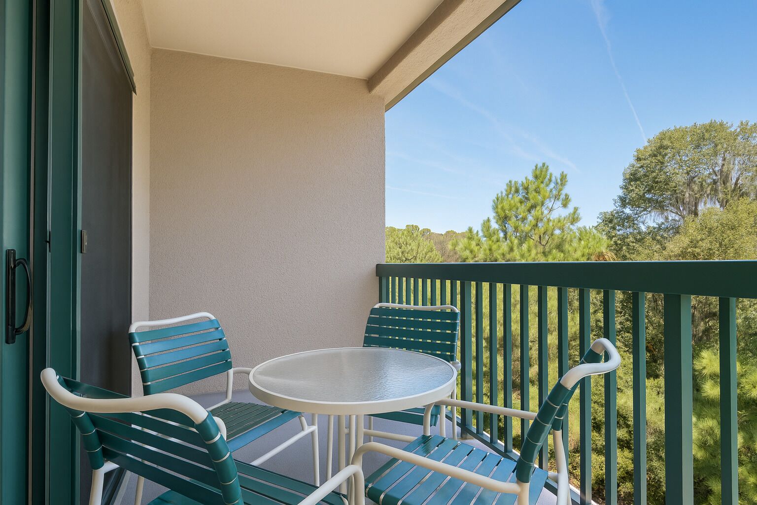 Un balcon avec une table et des chaises, une vue sur les arbres et la façade d’un immeuble.