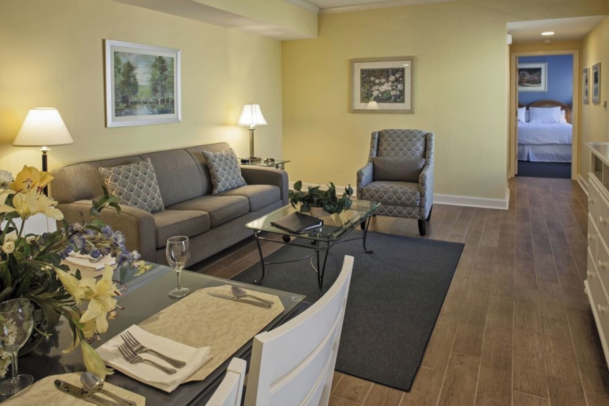 A hotel room with a sofa, armchair, dining table with cutlery, and a bed.