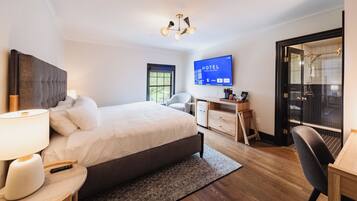 A hotel room with a bed, desk, chair, and a television displaying 'HOTEL STATE COLLEGE'.