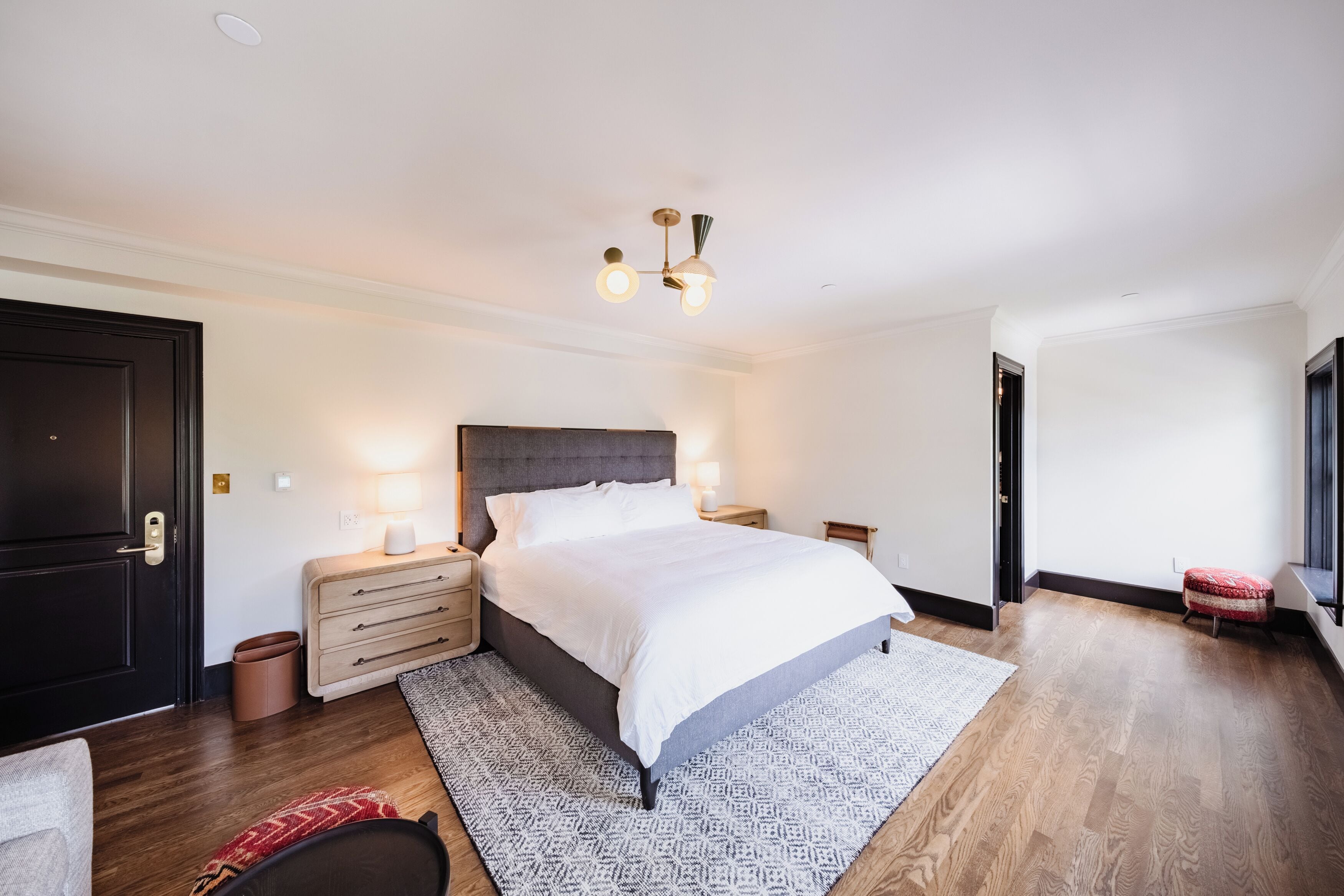 A modern bedroom with a large bed, bedside tables, a ceiling light fixture, and a small window.