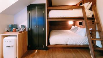 Une petite chambre avec un lit superposé, une kitchenette équipée d’un réfrigérateur et une armoire.