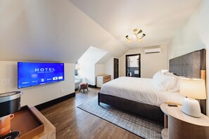 A hotel room with a large bed, a TV on the wall, a desk with a lamp, and a small table with a pot. - Hotel State College (State College)