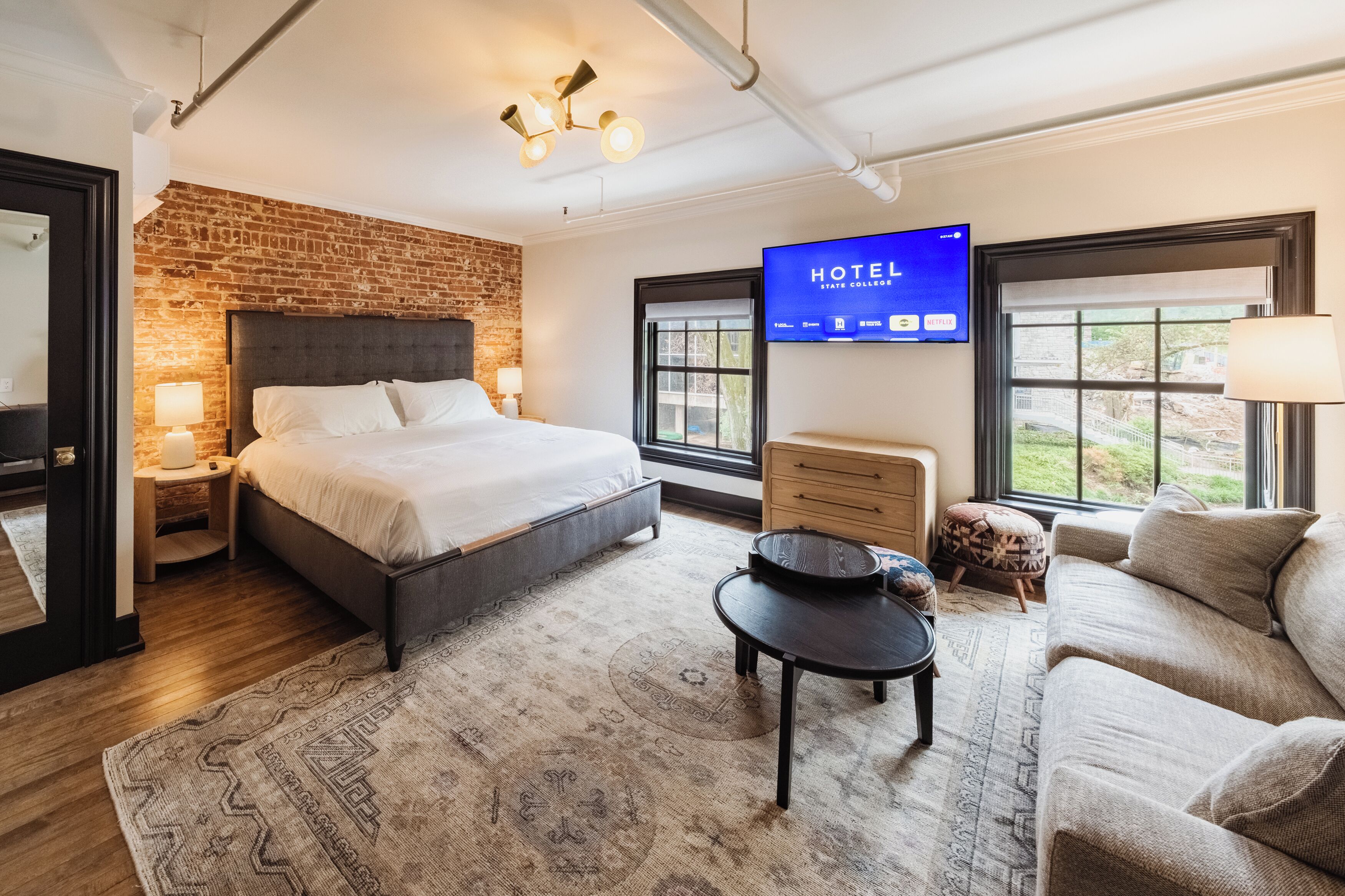 Una habitación de hotel con cama, televisión, sofá, mesa de centro y pared de ladrillo.