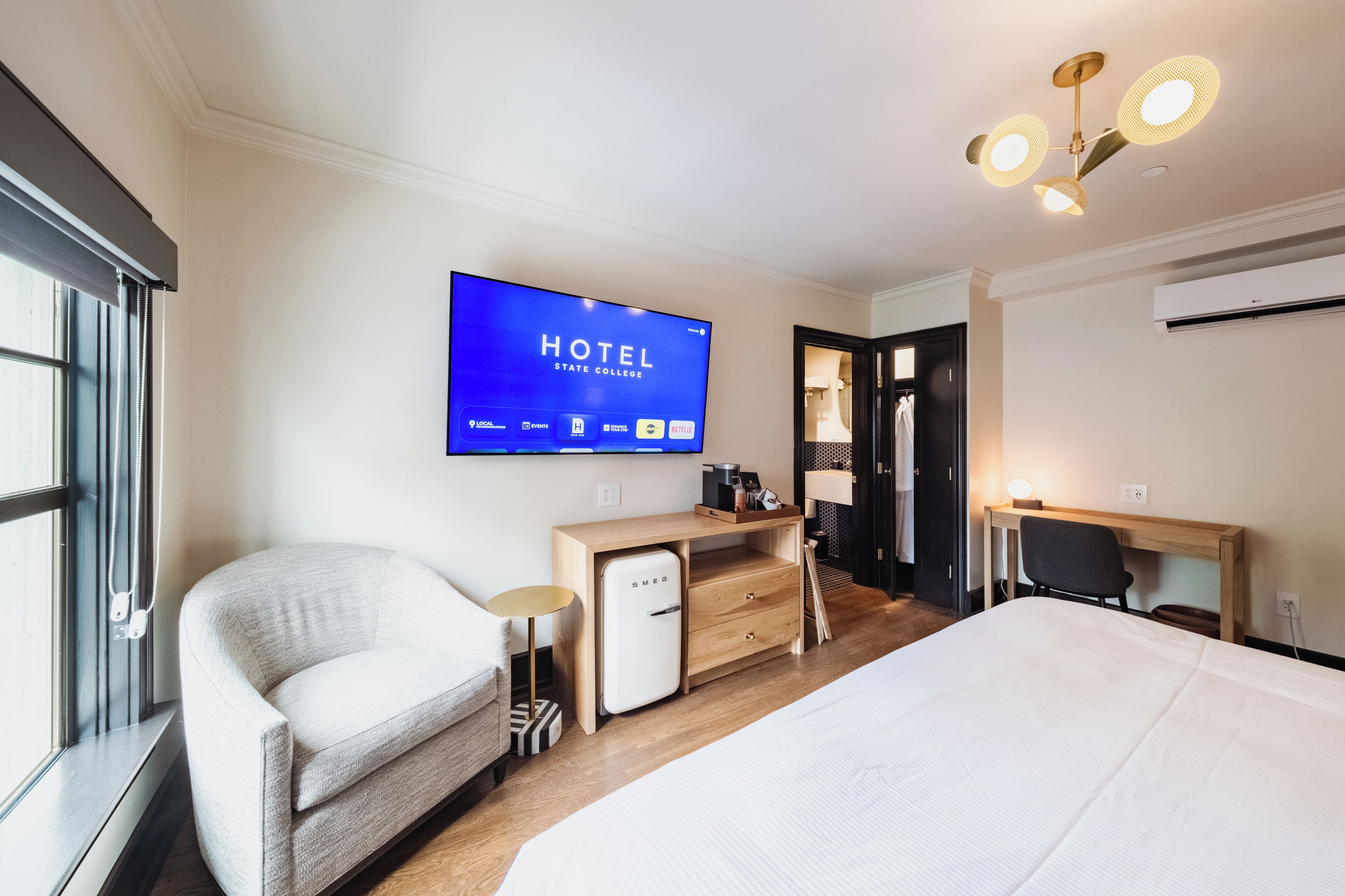 Habitación de hotel con cama, escritorio, silla, televisor mostrando el nombre del hotel y armario.