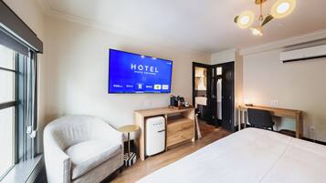 Habitación de hotel con cama, escritorio, silla, televisor mostrando el nombre del hotel y armario.