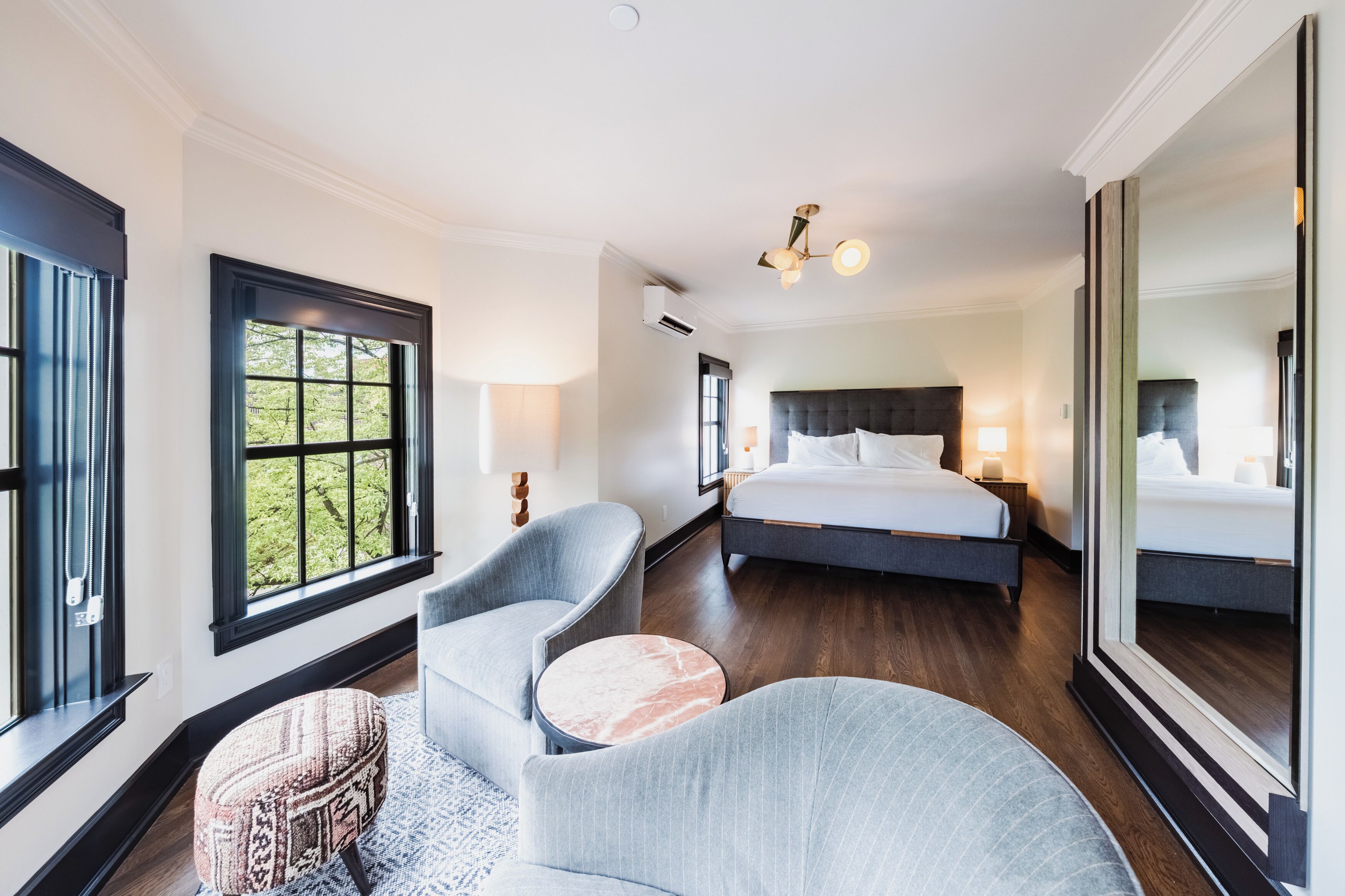 A bedroom with a large bed, a sitting area with a chair and ottoman, and a large mirror.