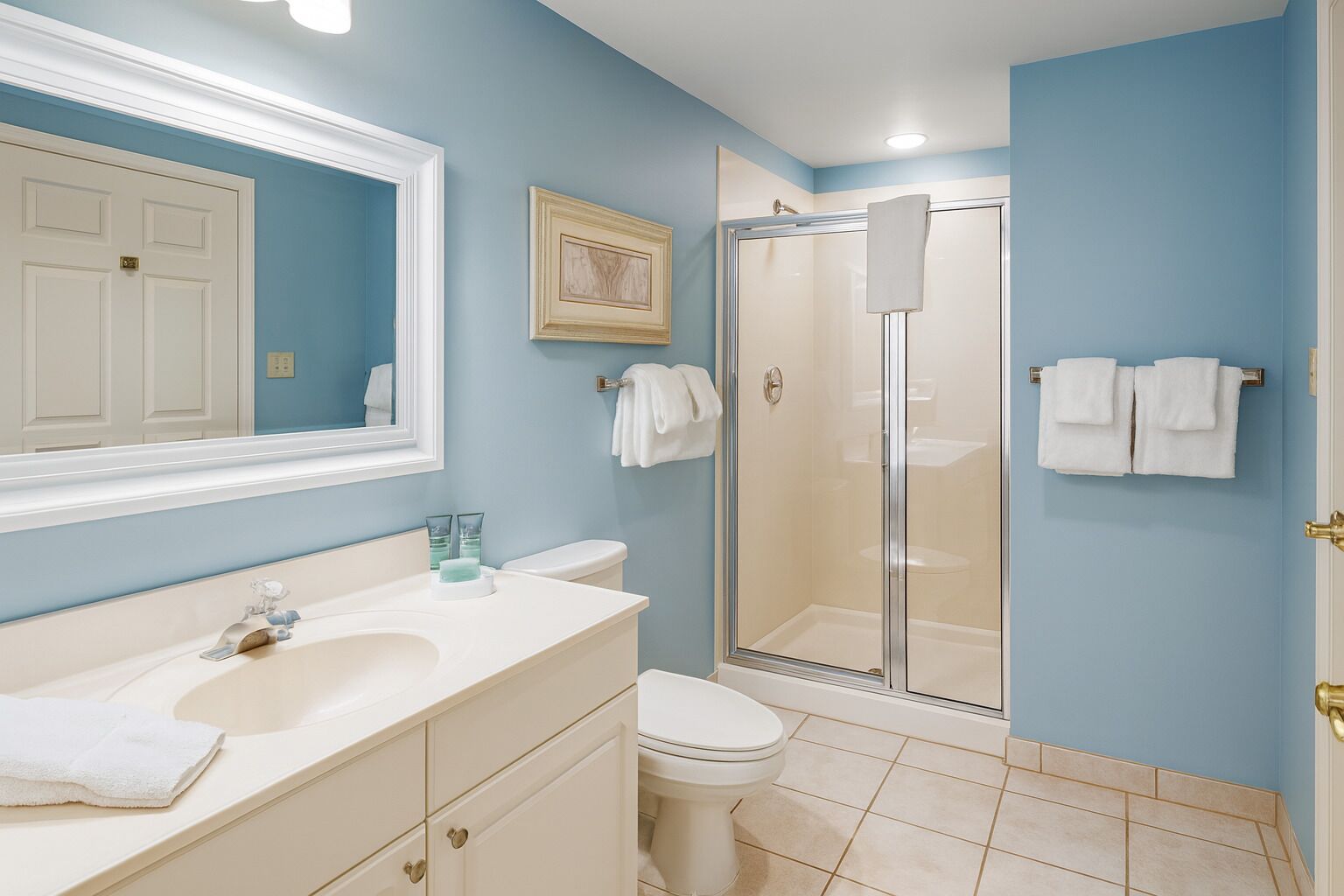 A bathroom with a white sink, a toilet, a shower with a glass door, and a mirror with a picture frame.