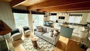 A cozy living room with a grey sofa, two armchairs, a coffee table, and a kitchen area with white cabinets and a microwave. - Hilltop's Cozy Cabin with Lakeviews, close to beach. Pet friendly (Windermere)