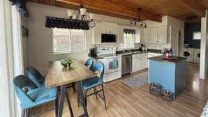 A modern kitchen with wooden ceiling beams, white cabinets, a central island, and blue chairs. - Hilltop's Cozy Cabin with Lakeviews, close to beach. Pet friendly (Windermere)