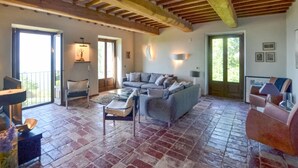 A spacious living room with a large grey sofa, a glass coffee table, and a dining area with a table and chairs. There is a balcony with a railing and a door leading outside. - Amazing home in Lisciano Niccone (Lisciano Niccone)