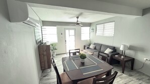 Un comedor con mesa de madera, sillas, ventilador de techo y un sofá.