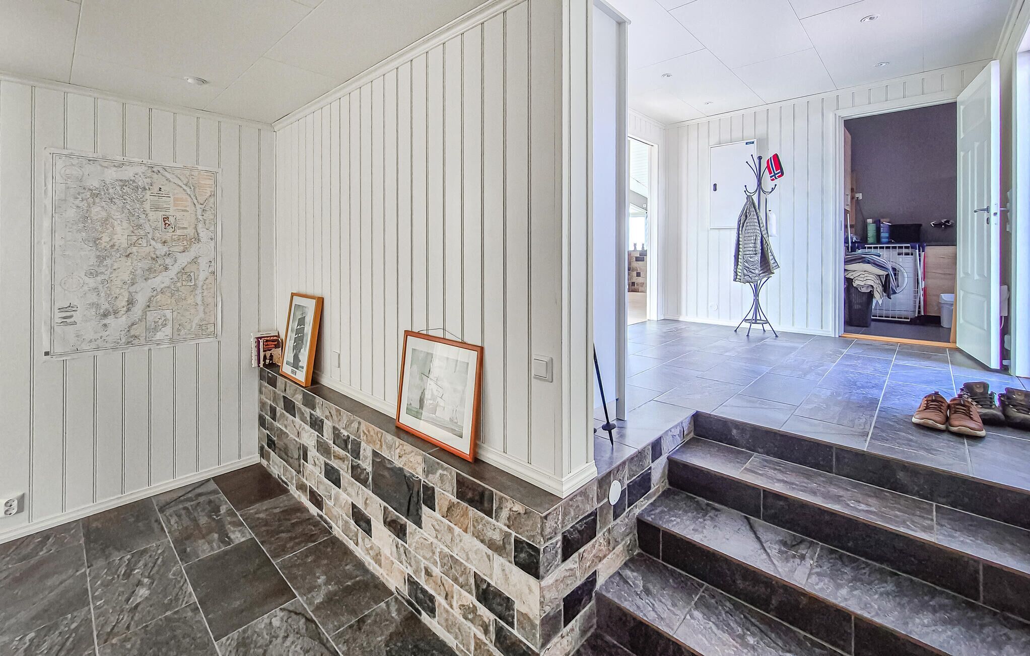A staircase with stone steps leading to a landing, a white wall with vertical paneling, and a door leading to another room.