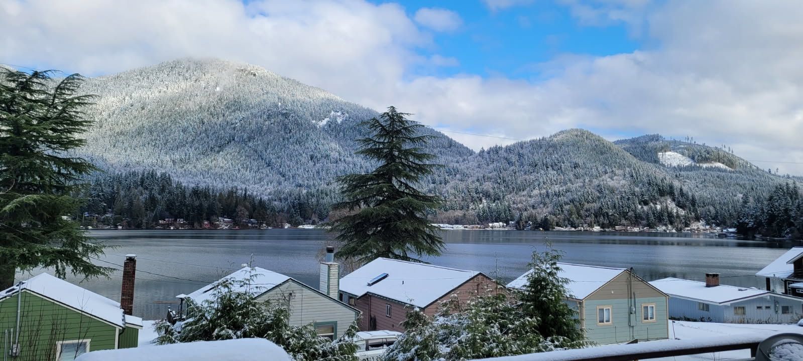 Vista de un lago con casas nevadas y montañas al fondo.