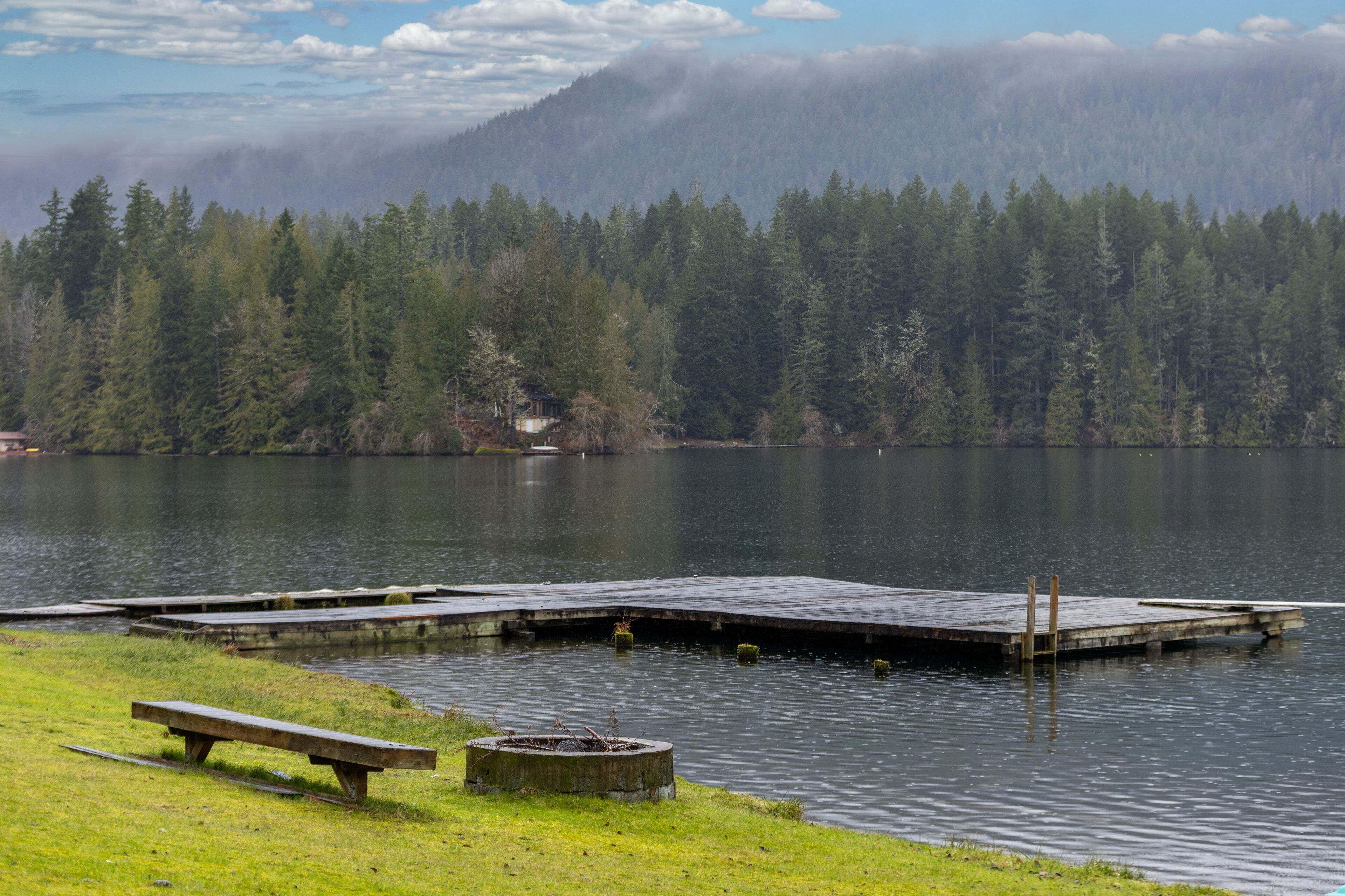 A lakeside dock with a wooden bench and a fire pit.