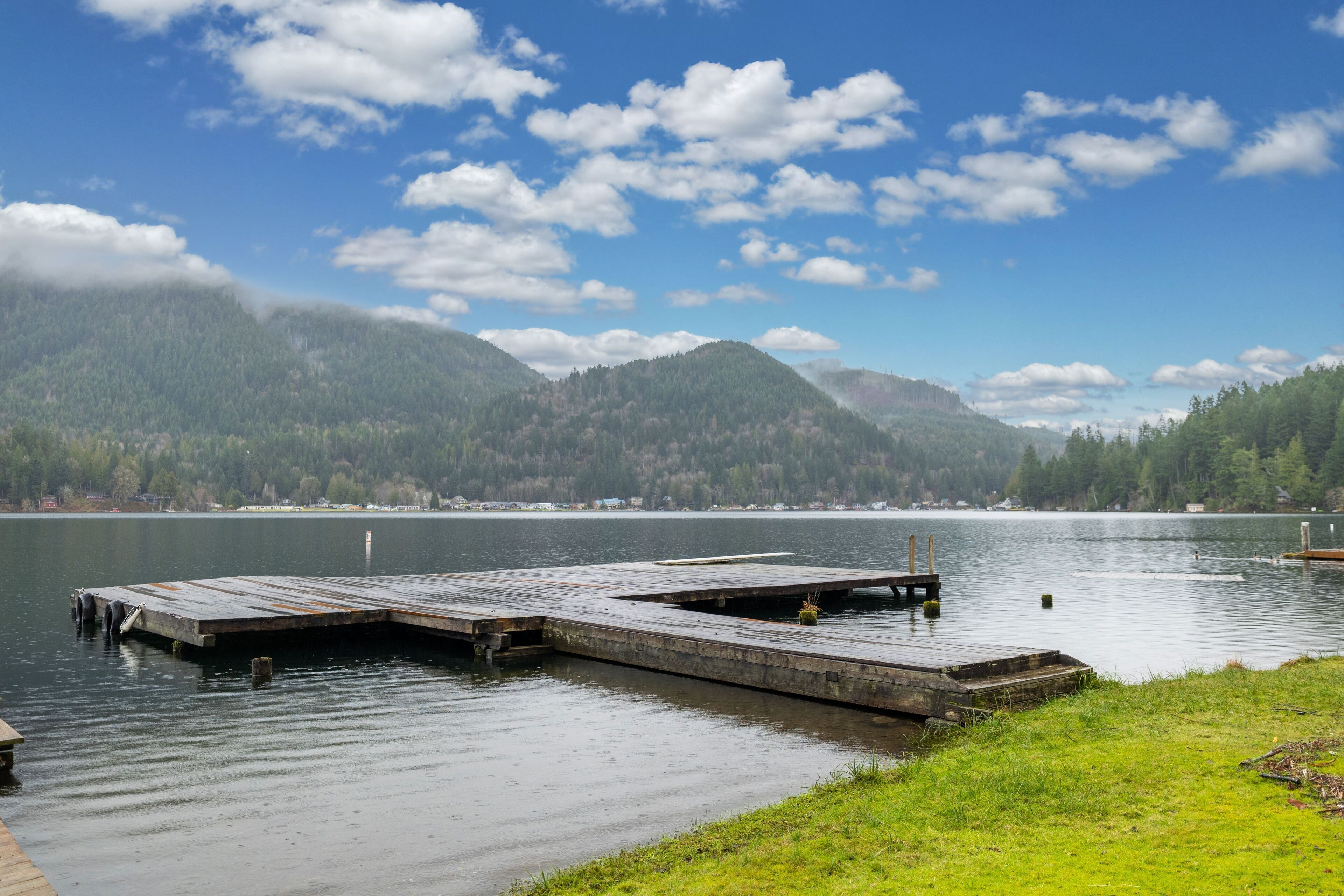 A wooden dock extending into calm water with a forested mountain backdrop.