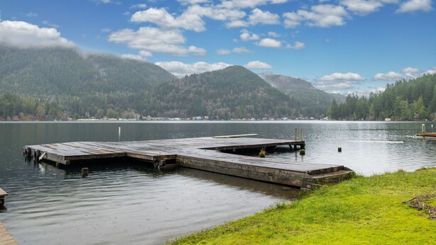 A wooden dock extending into calm water with a forested mountain backdrop. - Lake Sutherland Cabin w/ Dock Access & Kayaks (Port Angeles)