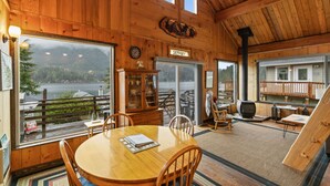 A wooden interior with a dining area, a fireplace, and a view of a lake. - Lake Sutherland Cabin w/ Dock Access & Kayaks (Port Angeles)