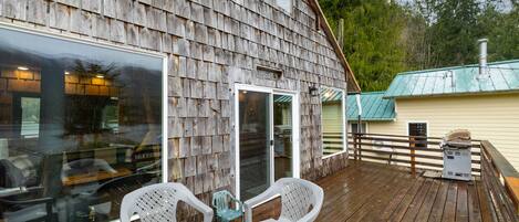 A wooden deck with a table and chairs, a glass door, and a metal heater.