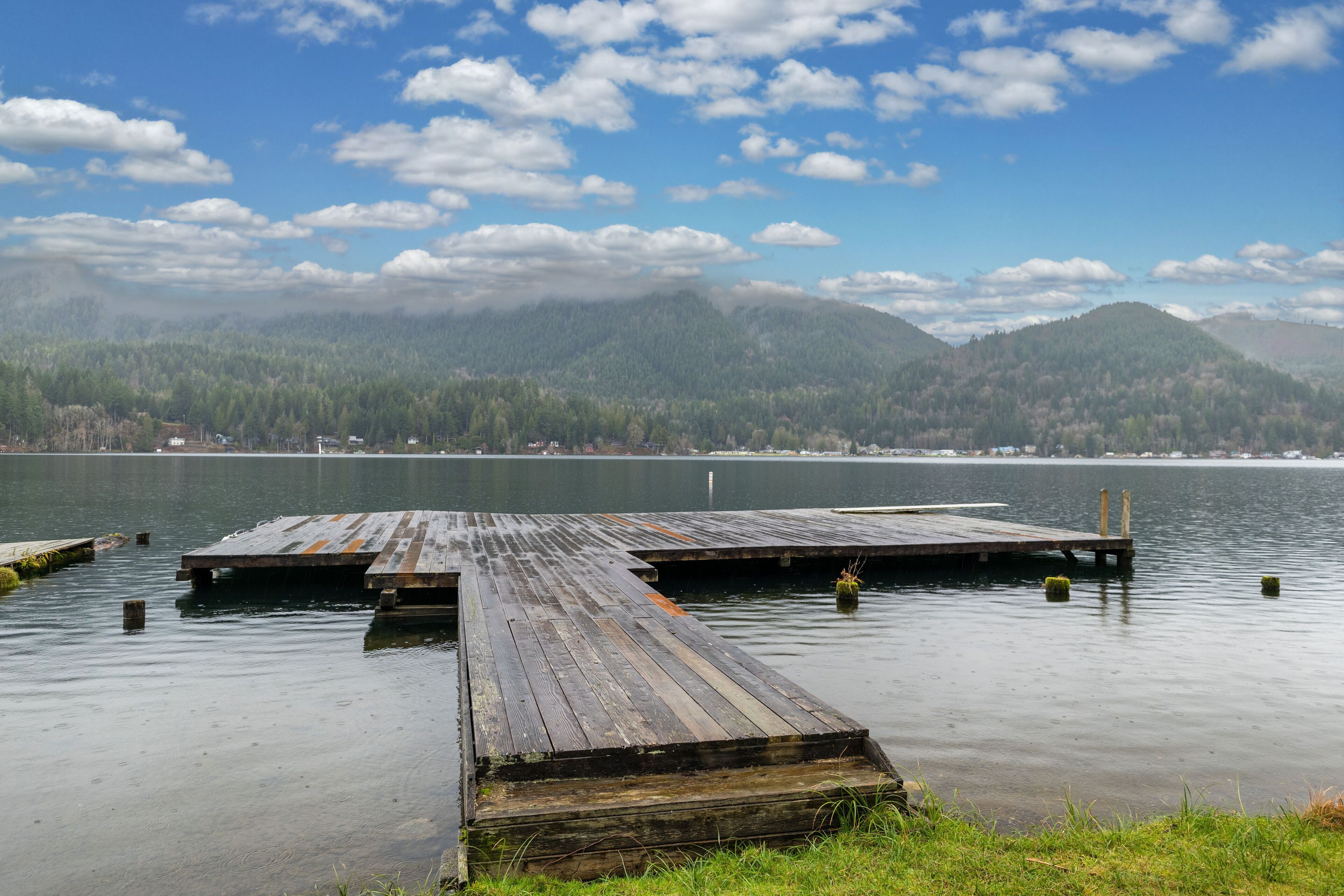 A wooden dock extending into calm water with a forested mountain range in the background.