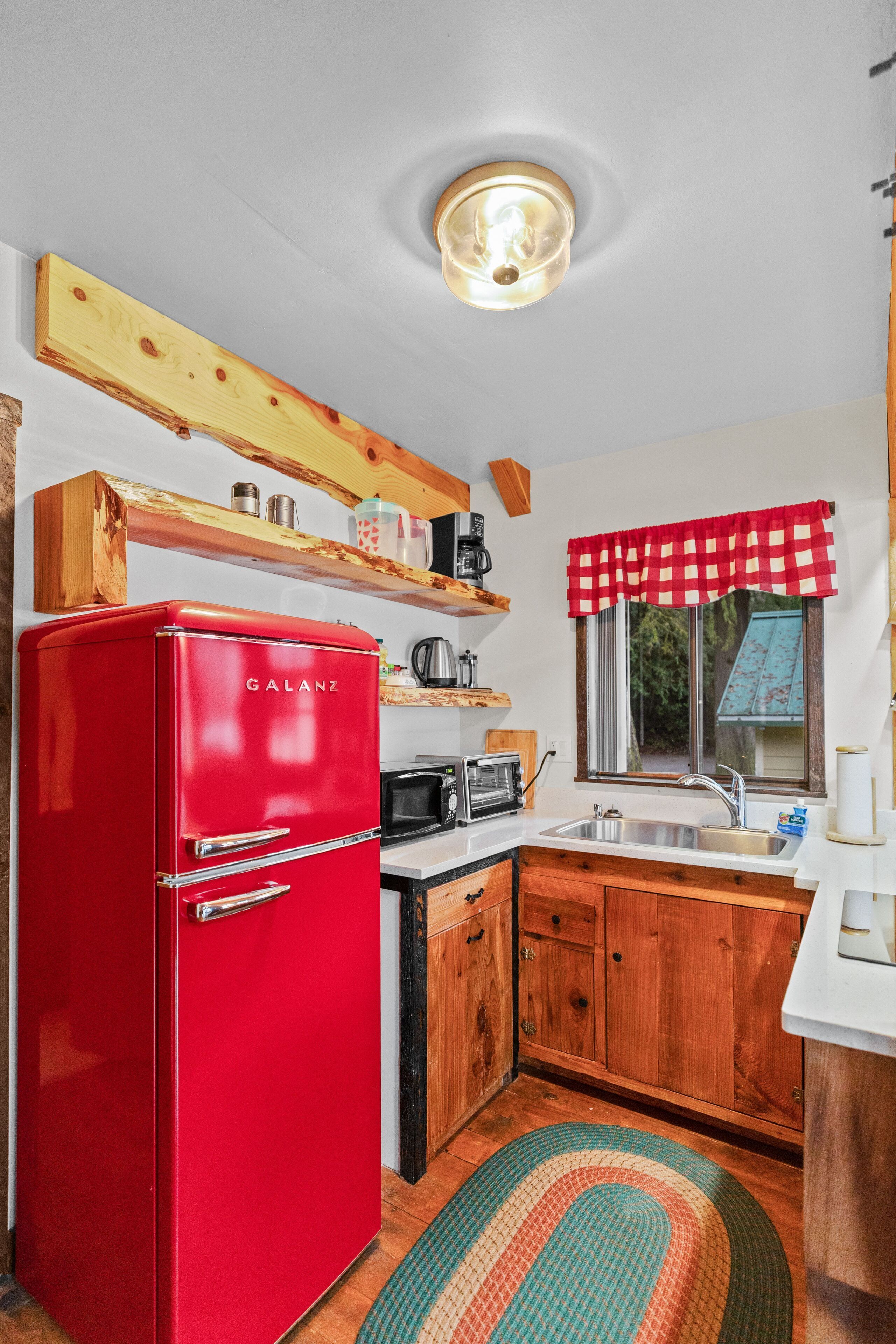 A compact kitchen with a red Galanz refrigerator, wooden cabinets, a microwave, and a sink.