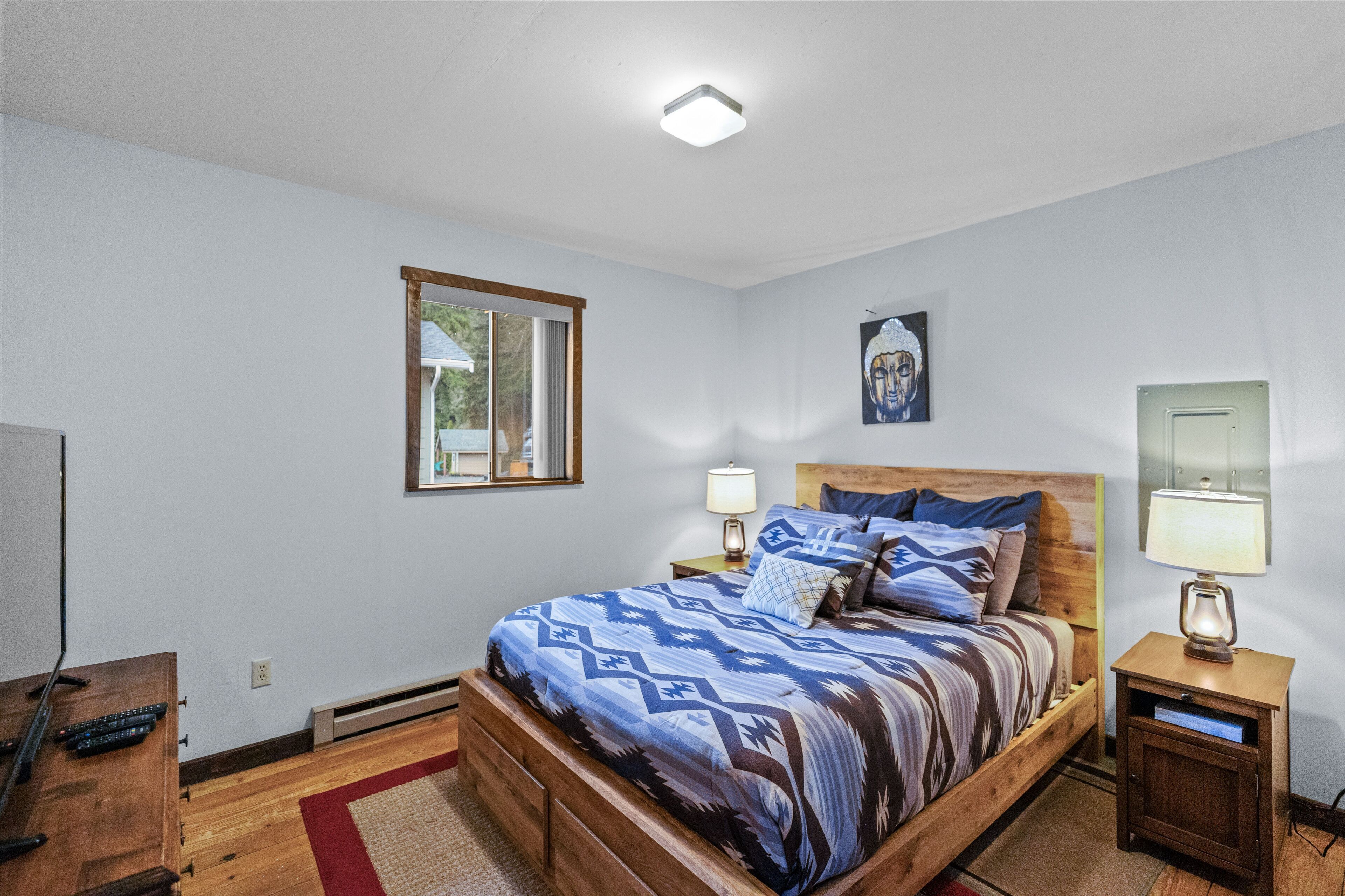 A bedroom with a wooden bed, two bedside tables with lamps, a window, and a painting on the wall.