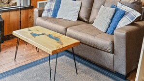 A cozy room with a wooden ceiling, a brown sofa, a small table, and framed pictures on the wall. - Lake Sutherland Cabin w/ Dock Access & Kayaks (Port Angeles)