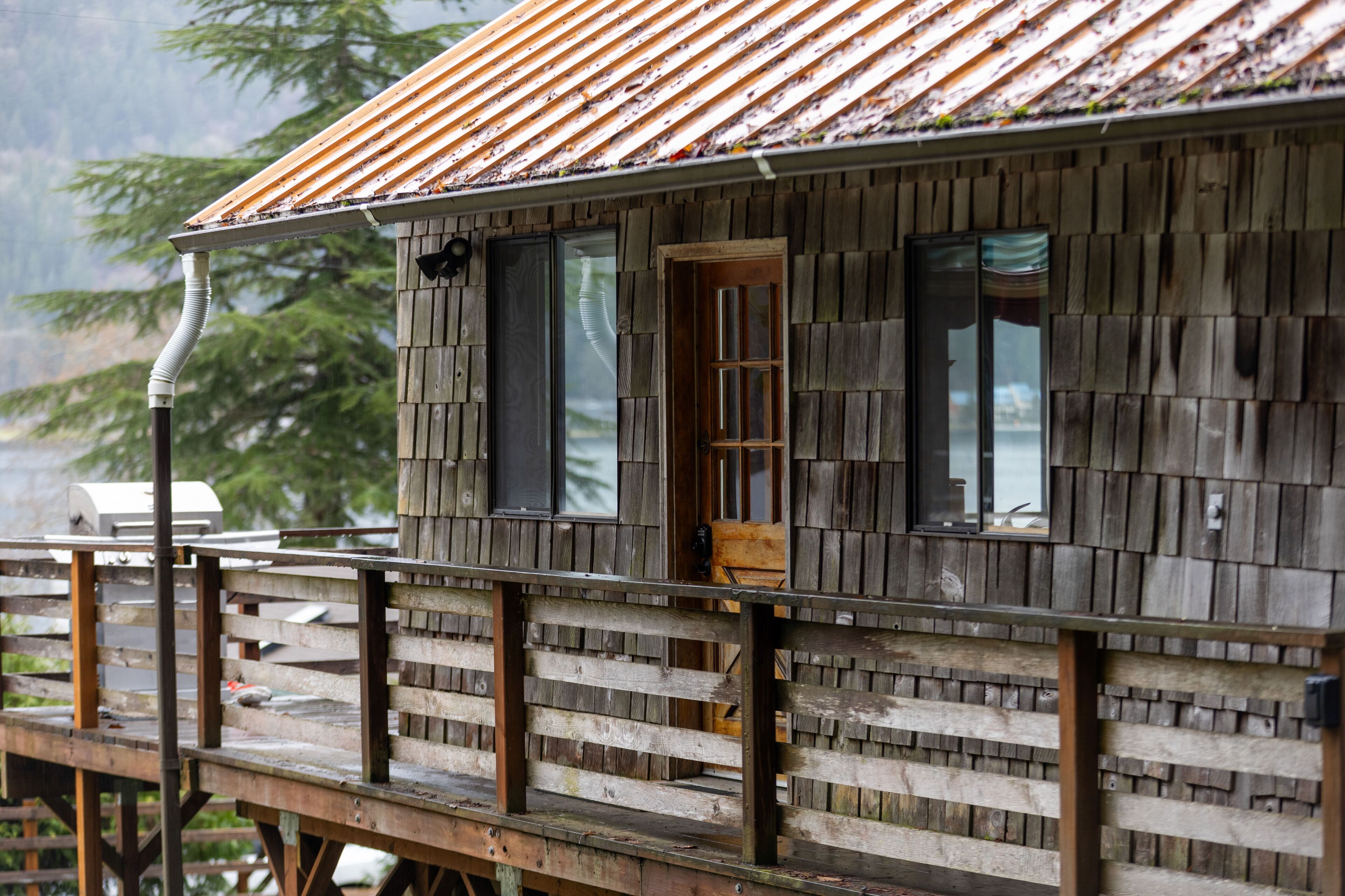 A wooden cabin with a metal roof, a deck, and a window overlooking a body of water.