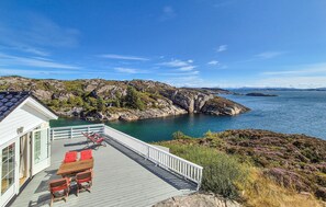 A coastal property with a wooden deck, outdoor seating, and a view of the sea and rocky landscape.