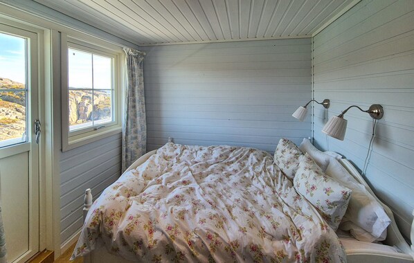 A bedroom with a bed, a window with curtains, and a wall-mounted lamp.