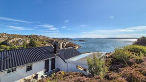 A coastal house with a tiled roof, a small porch, and a view of the sea and distant hills.
