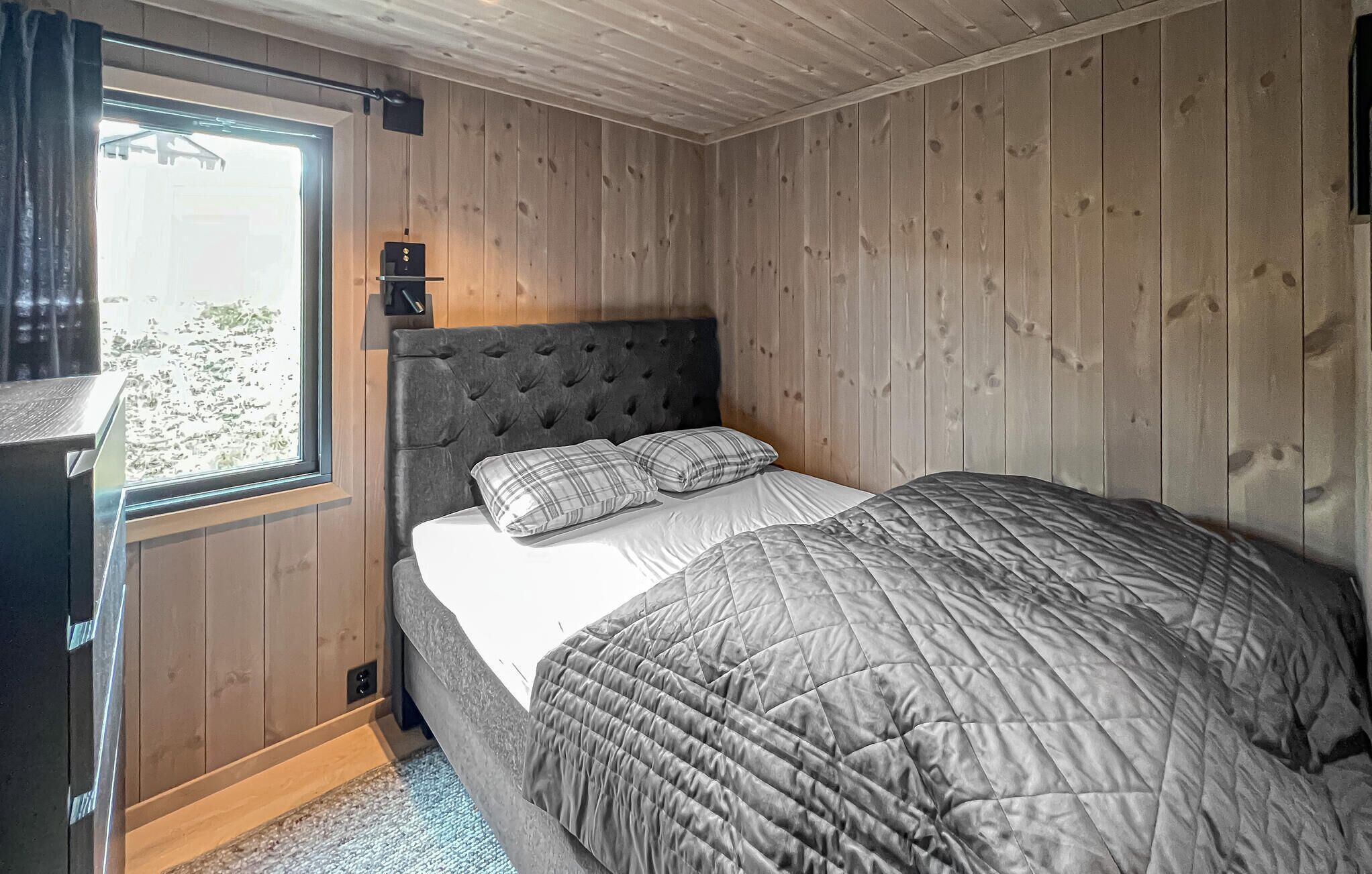Une chambre à coucher avec un grand lit, une tête de lit en bois et une fenêtre avec des rideaux.