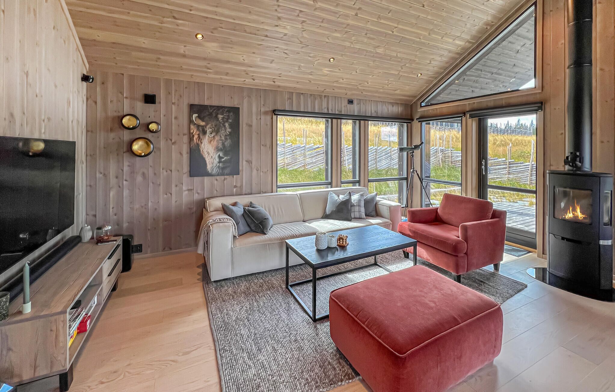 Een moderne woonkamer met een bank, een rode fauteuil, een salontafel, een televisie en een open haard.