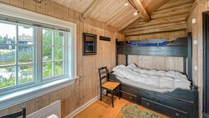 A cabin-style bedroom with a bunk bed, a wooden chair, a small table, and a view of the outdoors through a large window.
