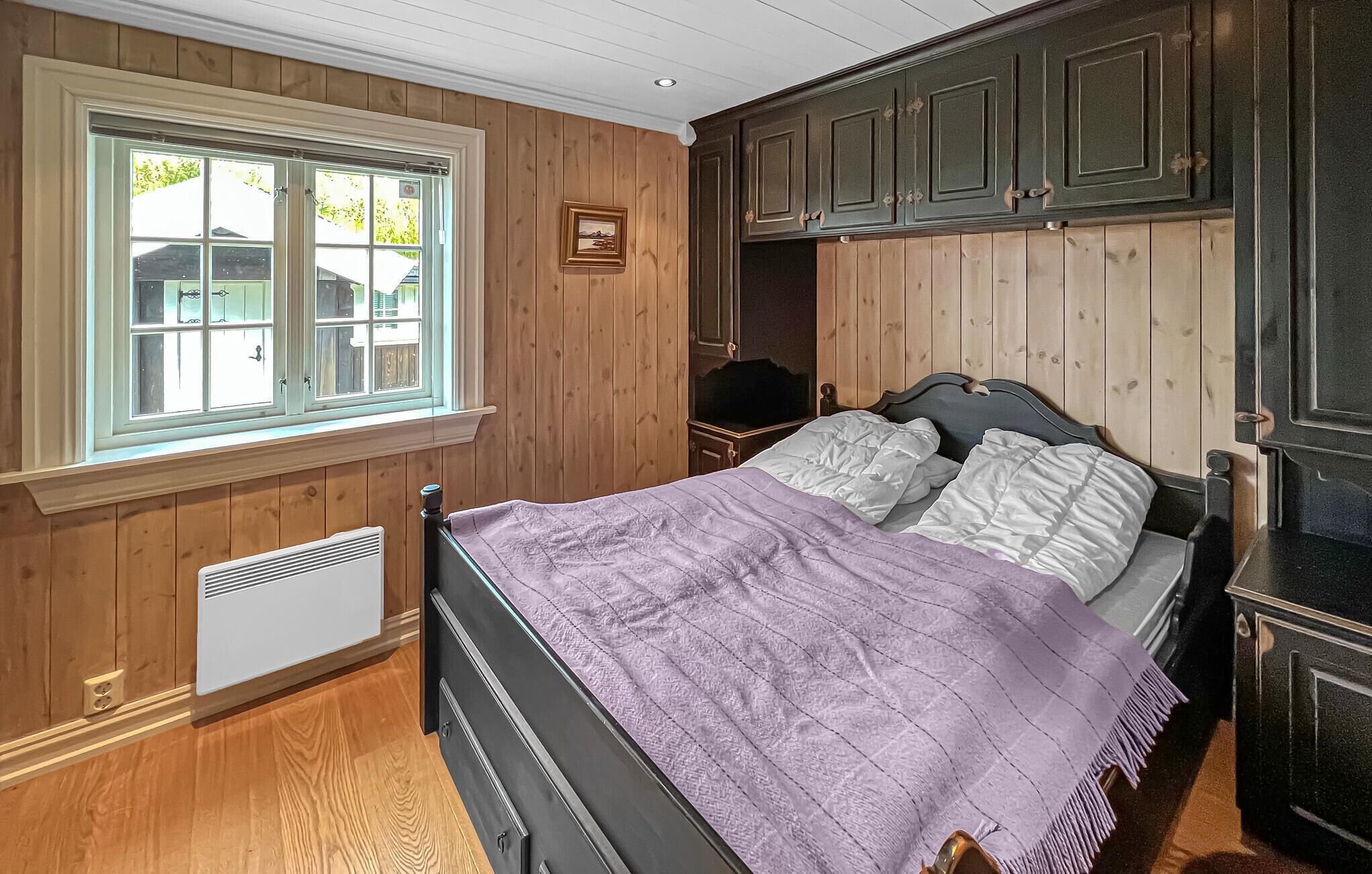 Een slaapkamer met een bed, houten wanden, een raam en een inbouwkast.