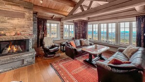 A cozy living room with a stone fireplace, leather sofas, and large windows offering a view of the landscape.