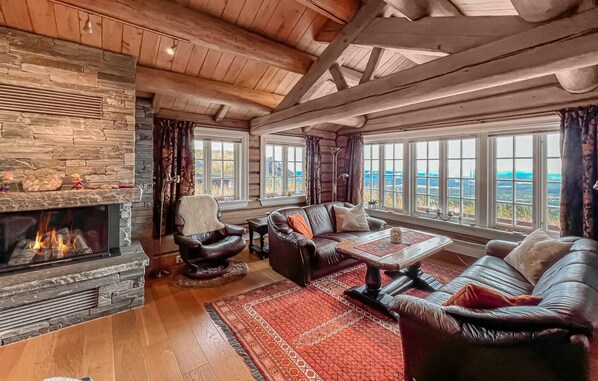 A cozy living room with a stone fireplace, leather sofas, and large windows offering a view of the landscape.