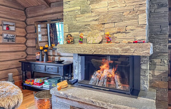 A log cabin interior with a stone fireplace, wooden walls, and a mirror.