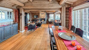 A spacious log cabin interior with a long dining table, wooden floors, and a fireplace.