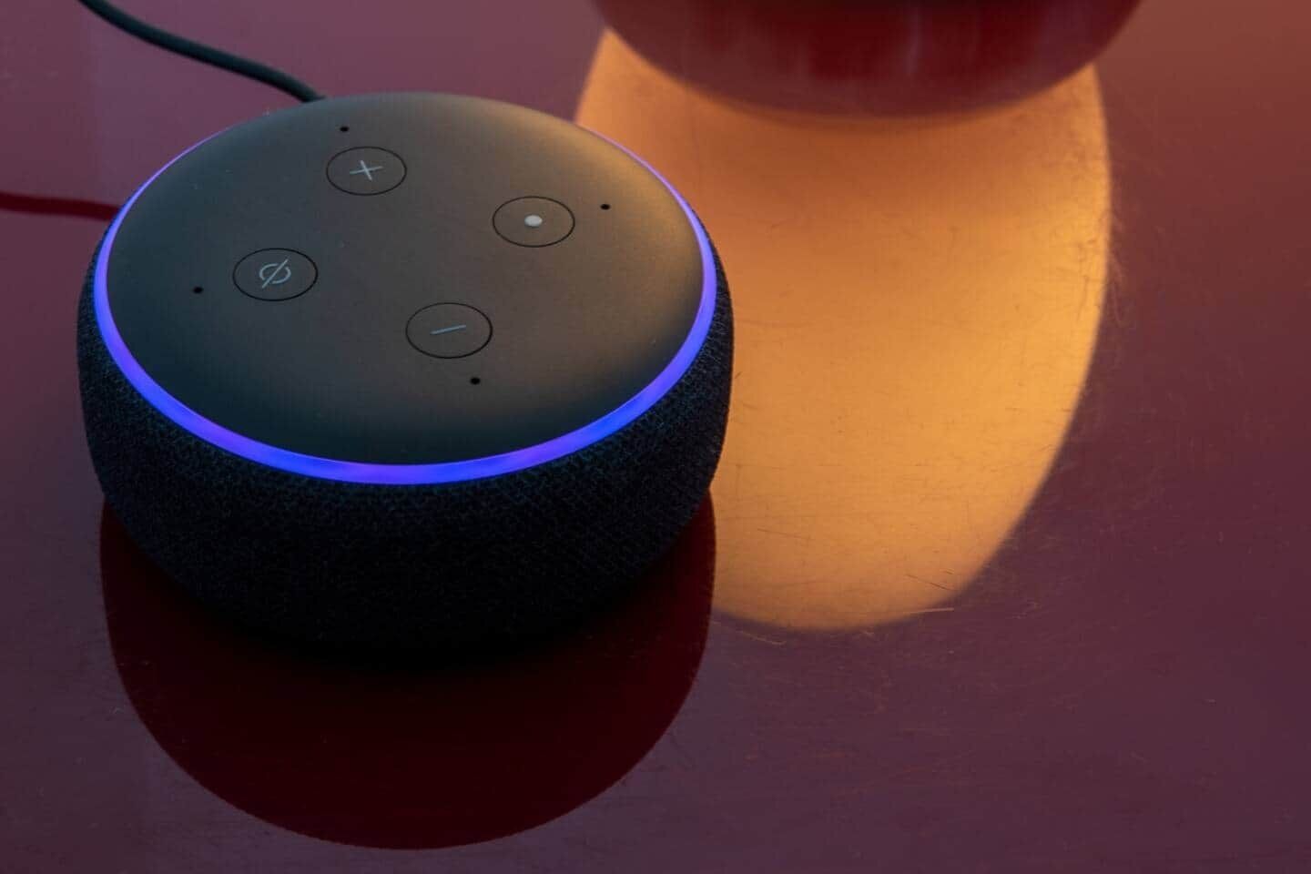 A smart speaker with a blue light ring, placed on a reflective surface.