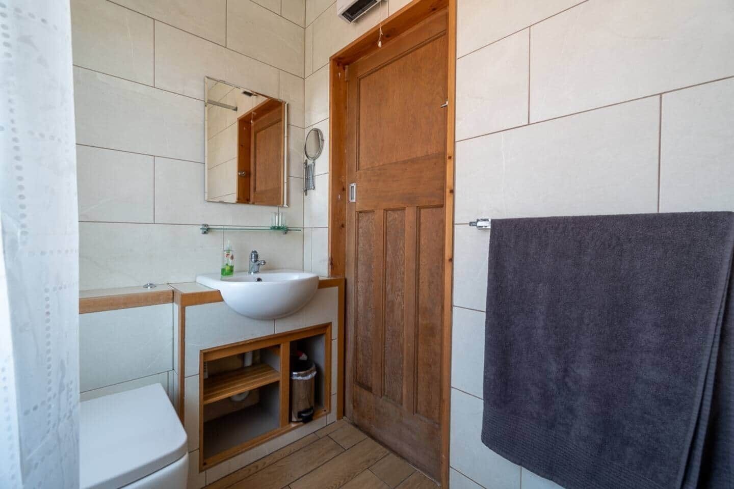 Een badkamer met een houten deur, een witte wastafel, een spiegel en een handdoek aan de muur.