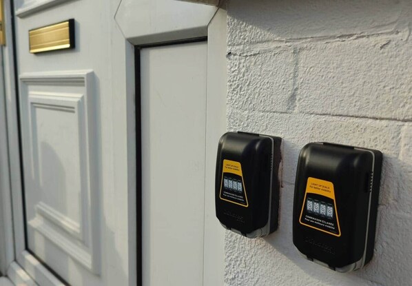 Two black intercoms mounted on a textured wall next to a white door with a brass plate.