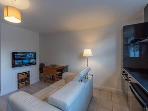 Una sala de estar moderna con un sofá, un televisor montado en la pared, una mesa de comedor y una lámpara.