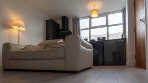 A living room with a sofa, a lamp, a kitchen area, and a large window. - Luxury modern flat • close to city • free parking (Leeds)