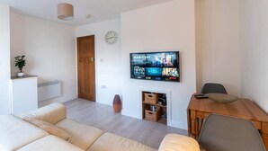 A modern living room with a flat-screen TV mounted on the wall, a wooden dining table, and a beige sofa. - Luxury modern flat • close to city • free parking (Leeds)